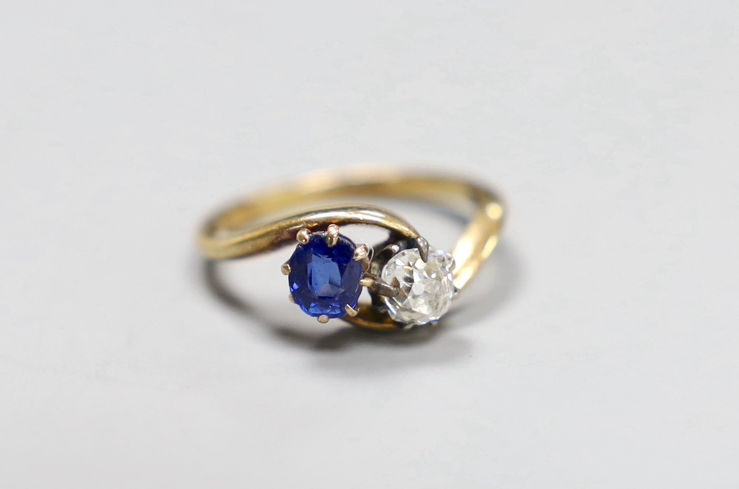 An early 20th century 18ct gold, sapphire and diamond two stone cross-over ring, size L, gross 3.2 grams